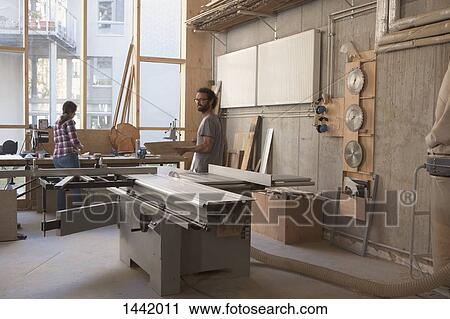 Stock Image - Male and female carpenters working in workshop. Fotosearch