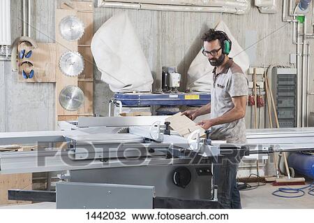 Stock Image - Male carpenter using a sliding table saw in workshop. Fotosearch