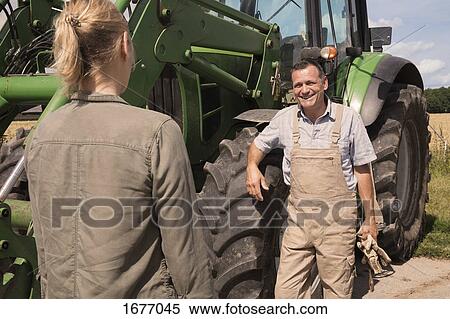 Male farmer talking to woman while standing by agricultural machinery on sunny day View Large Photo Image Stock Photography - Male farmer talking to woman while standing by agricultural machinery on sunny day. Fotosearch