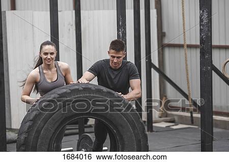 Male instructor assisting female athlete in flipping tire during crossfit training View Large Photo Image Stock Photograph - Male instructor assisting female athlete in flipping tire during crossfit training. Fotosearch