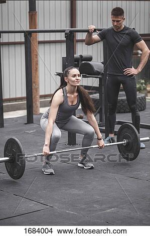 Male instructor looking at female athlete lifting barbell during cross training View Large Photo Image Picture - Male instructor looking at female athlete lifting barbell during cross training. Fotosearch