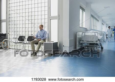 Stock Photo - Male patient reading magazine, waiting in hospital waiting room. Fotosearch