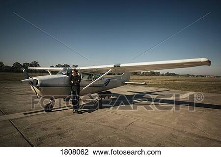 Stock Image - Male pilot standing at small propellor airplane on sunny tarmac. Fotosearch