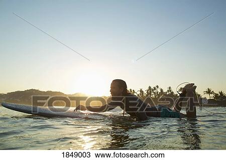 Stock Image - Male surfer paddling out on sunset ocean, Sayulita, Nayarit, Mexico. Fotosearch