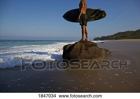 Male surfer with surfboard standing on large stone on beach, Sayulita, Nayarit, Mexico View Large Photo Image Picture - Male surfer with surfboard standing on large stone on beach, Sayulita, Nayarit, Mexico. Fotosearch