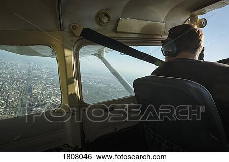 Stock Photograph - Man flying small airplane over city. Fotosearch