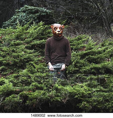 Stock Image - Man wearing bear mask while standing amidst plants. Fotosearch