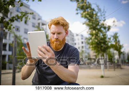 Stock Photo - Man with beard using digital tablet in city. Fotosearch