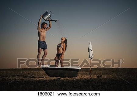 Man with watering can showering woman in bathtub in rural field View Large Photo Image Stock Image - Man with watering can showering woman in bathtub in rural field. Fotosearch
