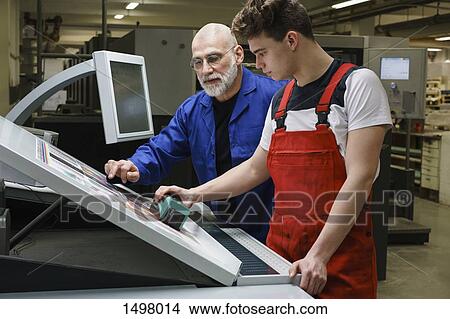 Mature man and coworker doing quality check of printout with machinery at printing press View Large Photo Image Picture - Mature man and coworker doing quality check of printout with machinery at printing press. Fotosearch
