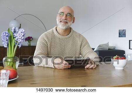Mature man holding digital tablet and looking away at home View Large Photo Image Stock Image - Mature man holding digital tablet and looking away at home. Fotosearch