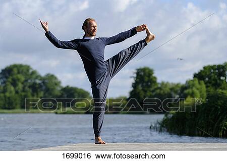 Mature man practicing yoga on pier by lake against sky View Large Photo Image Stock Photograph - Mature man practicing yoga on pier by lake against sky. Fotosearch