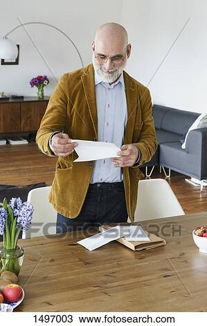 Mature man reading letter by table at home View Large Photo Image Stock Image - Mature man reading letter by table at home. Fotosearch