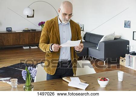 Mature man standing by table and reading letter at home View Large Photo Image Stock Photograph - Mature man standing by table and reading letter at home. Fotosearch