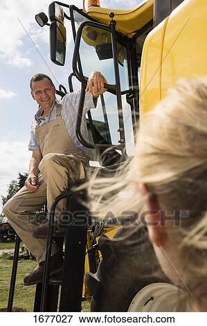 Mature man talking to woman while sitting on tractor at farm View Large Photo Image Stock Photo - Mature man talking to woman while sitting on tractor at farm. Fotosearch