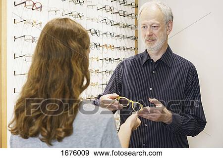 Stock Photo - Mature owner showing eyeglasses to woman with brown hair at store. Fotosearch