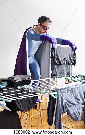 Mature superhero drying laundry on rack against white wall View Large Photo Image Stock Image - Mature superhero drying laundry on rack against white wall. Fotosearch
