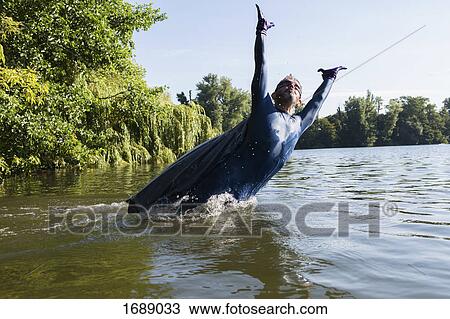 Mature superhero jumping with arms raised in river against sky View Large Photo Image Stock Image - Mature superhero jumping with arms raised in river against sky. Fotosearch