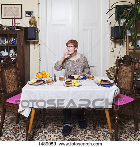 Mature woman cupping hand at mouth while having food at table View Large Photo Image Stock Photo - Mature woman cupping hand at mouth while having food at table. Fotosearch