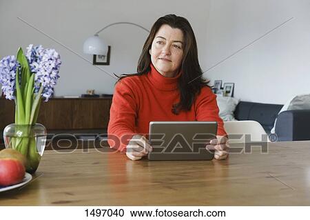 Mature woman looking away while holding digital tablet on table at home View Large Photo Image Stock Image - Mature woman looking away while holding digital tablet on table at home. Fotosearch
