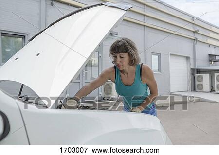 Mature woman repairing car against building View Large Photo Image Stock Photo - Mature woman repairing car against building. Fotosearch
