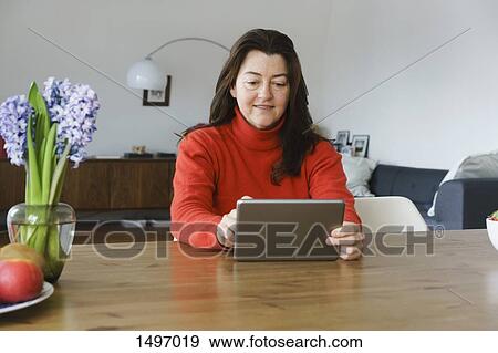Mature woman using digital tablet on table at home View Large Photo Image Stock Photo - Mature woman using digital tablet on table at home. Fotosearch