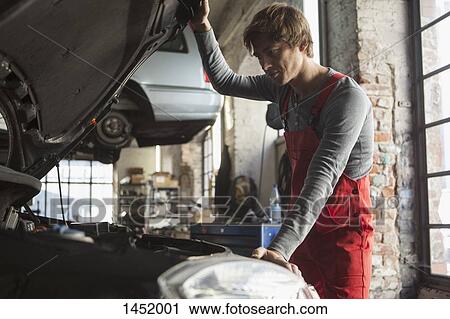 Stock Image - Mechanic examining car engine at garage. Fotosearch