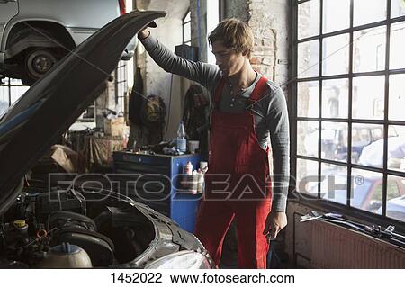 Stock Image - Mechanic examining car engine at repair shop. Fotosearch