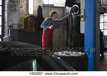 Mechanic examining car while holding clipboard at garage View Large Photo Image Stock Photo - Mechanic examining car while holding clipboard at garage. Fotosearch