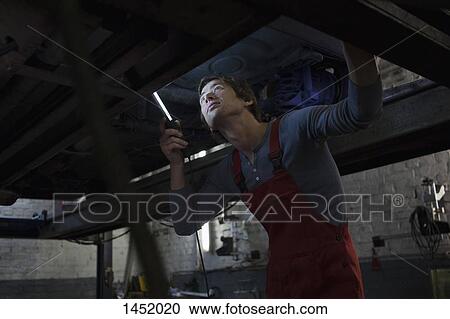 Stock Image - Mechanic examining underneath car at garage. Fotosearch