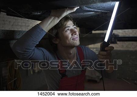 Picture - Mechanic holding illuminated fluorescent light while examining car. Fotosearch