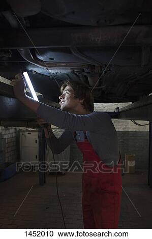 Stock Image - Mechanic holding illuminated fluorescent light while examining underneath car. Fotosearch