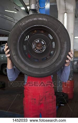 Mechanic holding tire in front of face at workshop View Large Photo Image Stock Image - Mechanic holding tire in front of face at workshop. Fotosearch