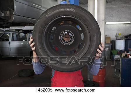 Mechanic holding tire in front of face at garage View Large Photo Image Stock Photography - Mechanic holding tire in front of face at garage. Fotosearch