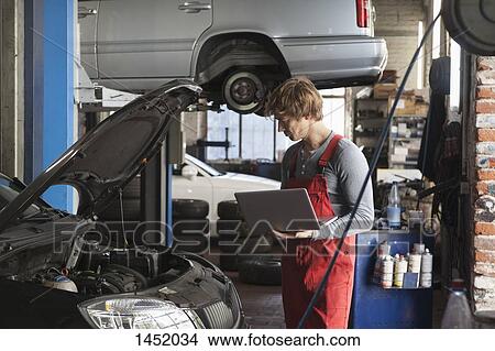 Mechanic using laptop while examining car engine at garage View Large Photo Image Picture - Mechanic using laptop while examining car engine at garage. Fotosearch