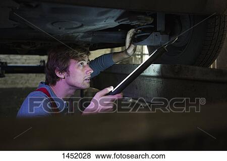 Stock Photo - Mechanic with illuminated fluorescent light examining car from below. Fotosearch