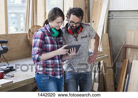 Stock Image - Mid adult carpenters using digital tablet in workshop. Fotosearch