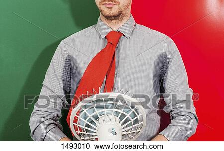 Stock Image - Midsection of businessman with sweaty armpits holding fan against colored background. Fotosearch