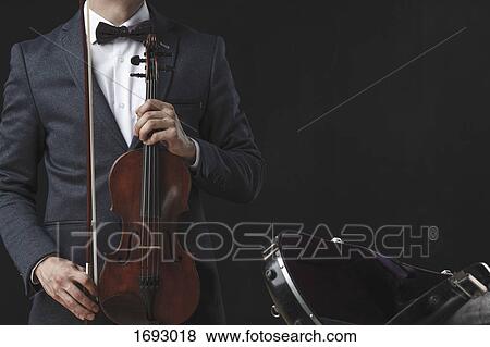 Stock Photo - Midsection of man holding violin while standing by case against black background. Fotosearch