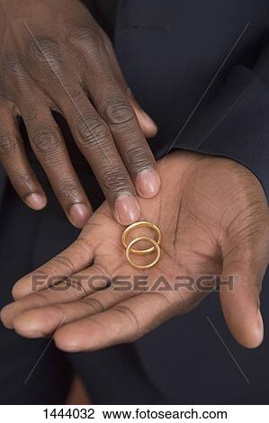 Stock Image - Midsection of man holding wedding rings. Fotosearch
