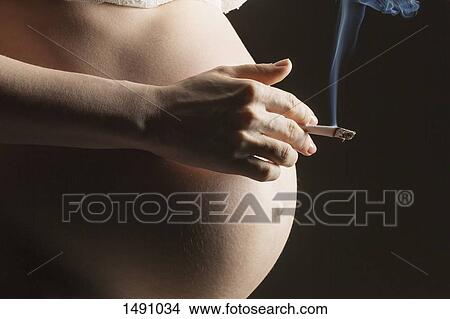 Picture - Midsection of pregnant woman smoking cigarette against gray background. Fotosearch