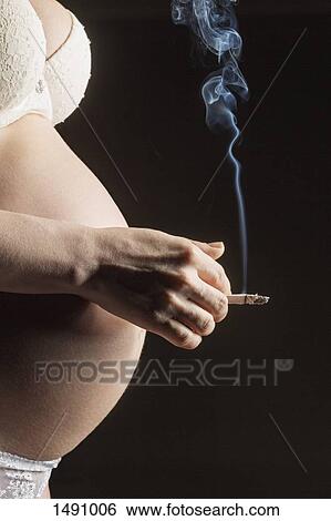 Stock Photograph - Midsection of pregnant woman smoking cigarette against gray background. Fotosearch