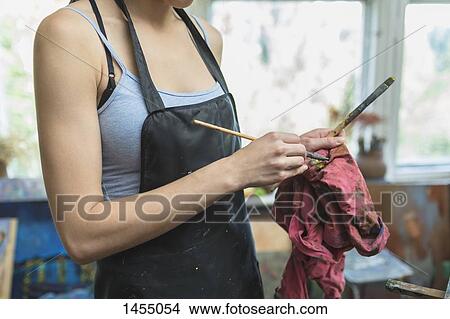 Picture - Midsection of woman cleaning paintbrush with fabric in studio. Fotosearch