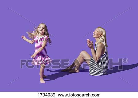 Mother watching daughter dancing on purple background View Large Photo Image Stock Photo - Mother watching daughter dancing on purple background. Fotosearch