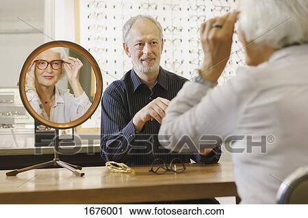 Stock Image - Optician assisting senior woman in choosing eyeglasses at store. Fotosearch