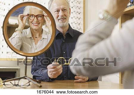 Picture - Optician assisting smiling woman in choosing eyeglasses at store. Fotosearch