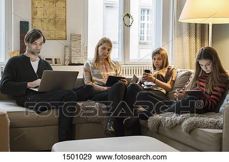 Parents and daughters using laptop and mobile devices on sofa in living room View Large Photo Image Stock Photo - Parents and daughters using laptop and mobile devices on sofa in living room. Fotosearch