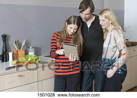 Stock Photo - Parents with daughter cooking while using digital tablet in kitchen. Fotosearch