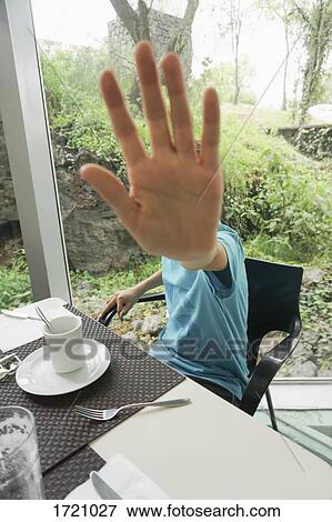 Stock Photo - Person showing stop gesture while sitting at table in restaurant. Fotosearch