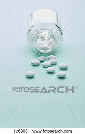 Stock Image - Pills spilling out from bottle on blue background. Fotosearch